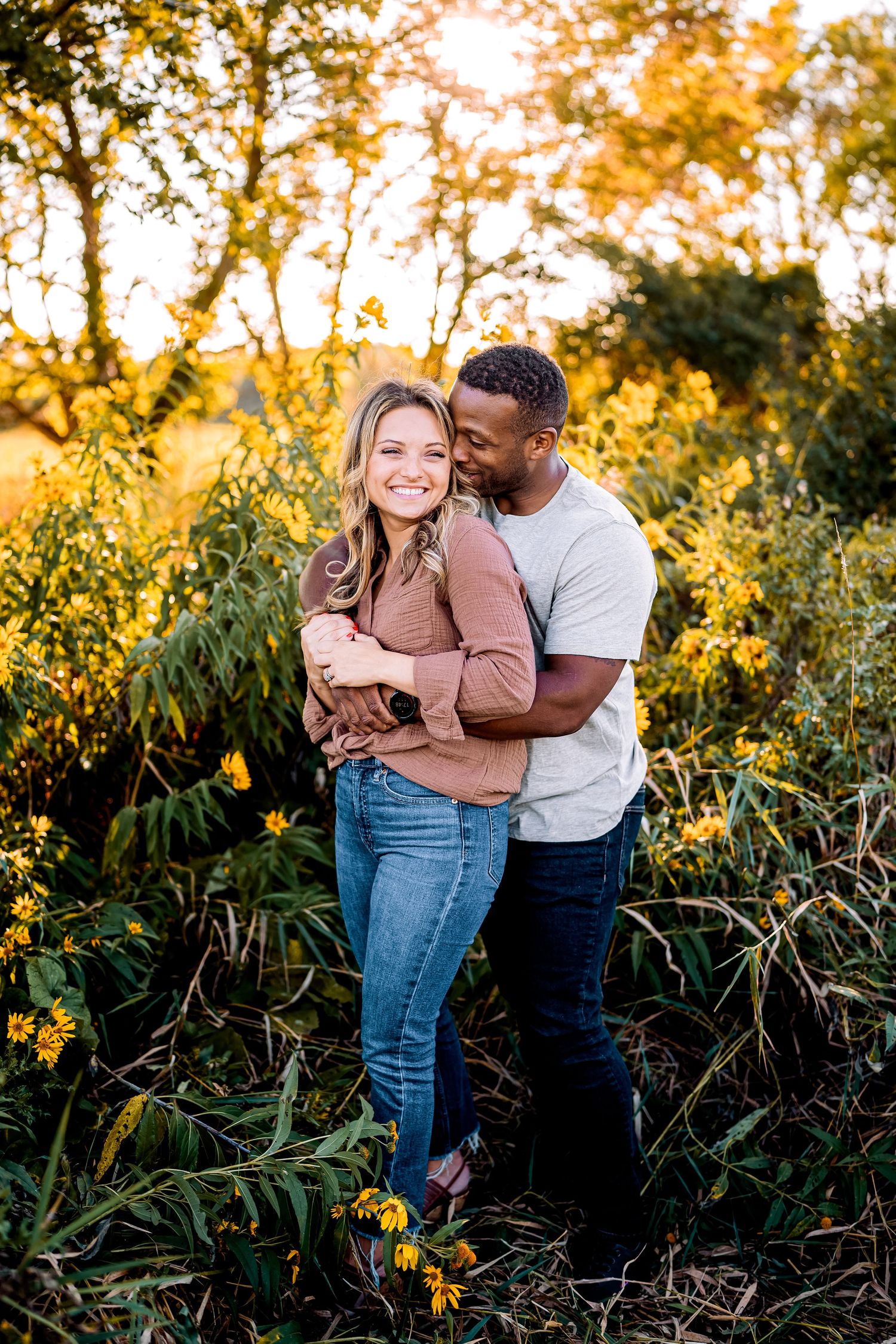 A couple shares an intimate moment while standing among yellow flowers at golden hour.
