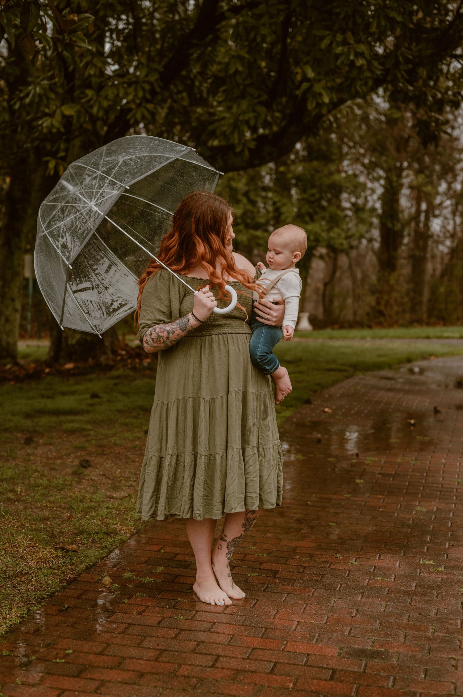a mom and her son stand together on wet brick path during rainstorm holding clear umbrella in autumn. photo by Samantha Campbell imagery