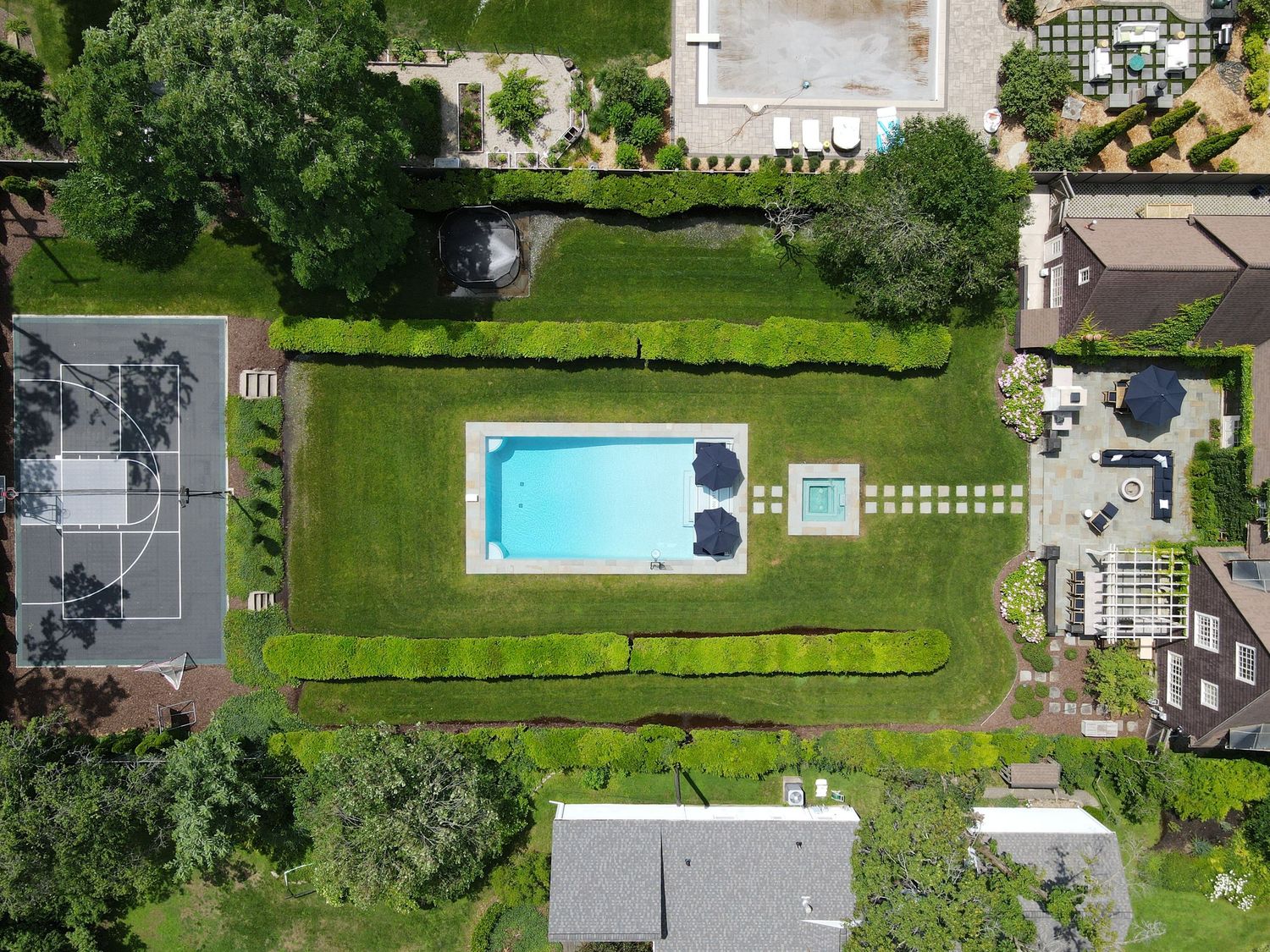 Aerial view of a luxury backyard with pool, spa, patio, basketball court, and lush landscaping for outdoor living.