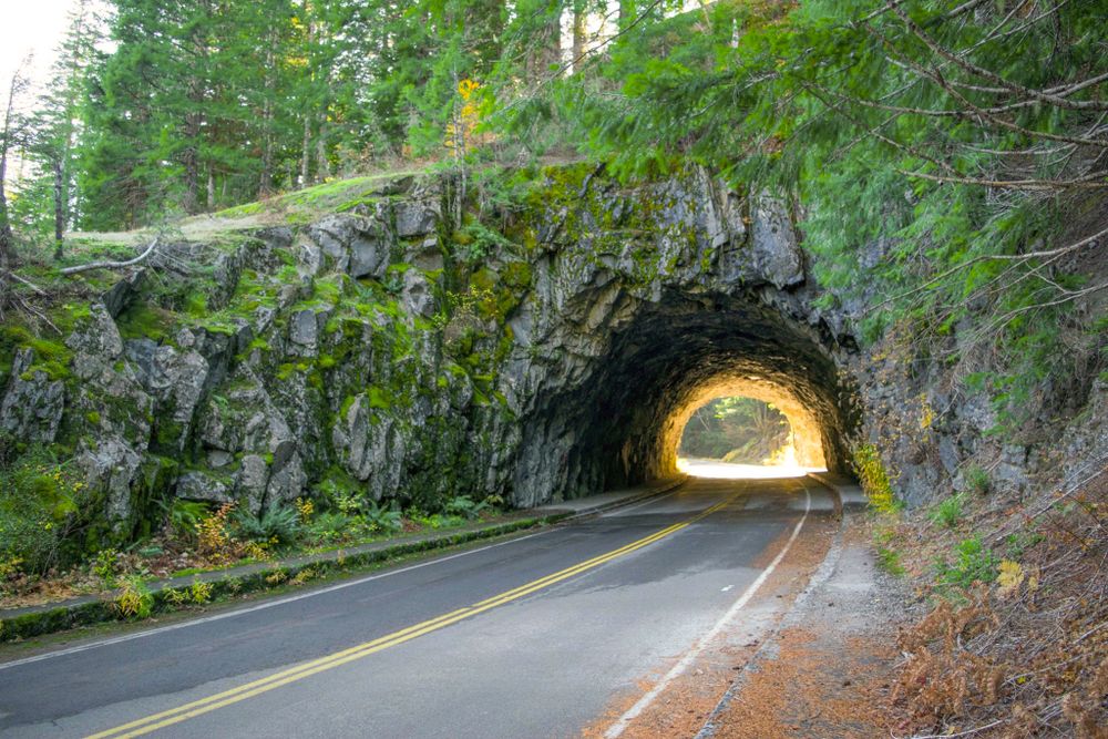 Scenic rock tunnel carved through a mountain with warm light glowing at the exit.
