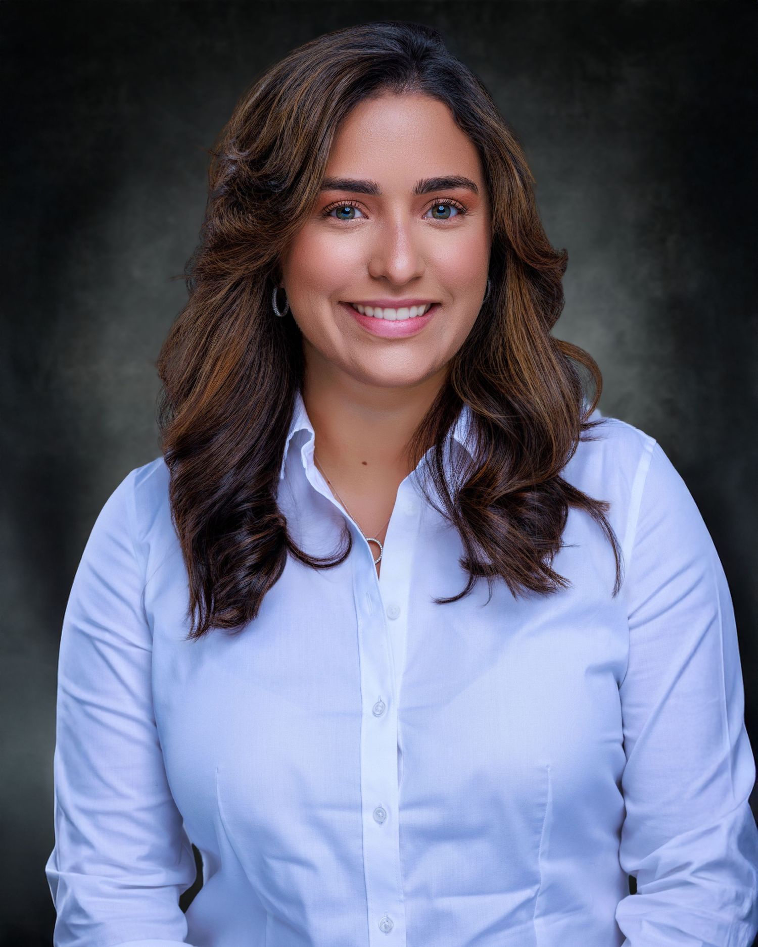 Professional headshot of a smiling woman with shoulder-length brown hair, wearing a blue blouse against a neutral background.