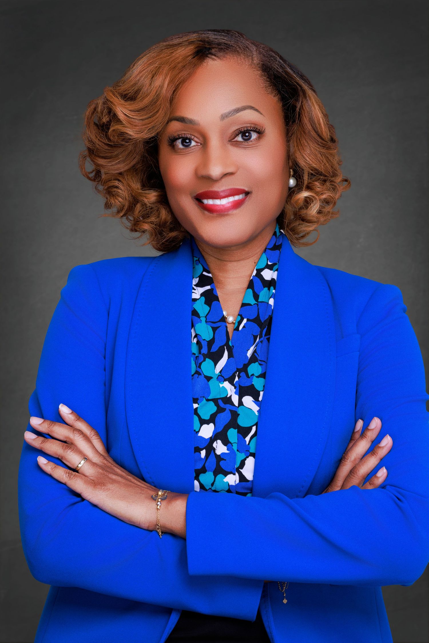 Professional headshot of a smiling woman with shoulder-length brown hair, wearing a blue blouse against a neutral background.