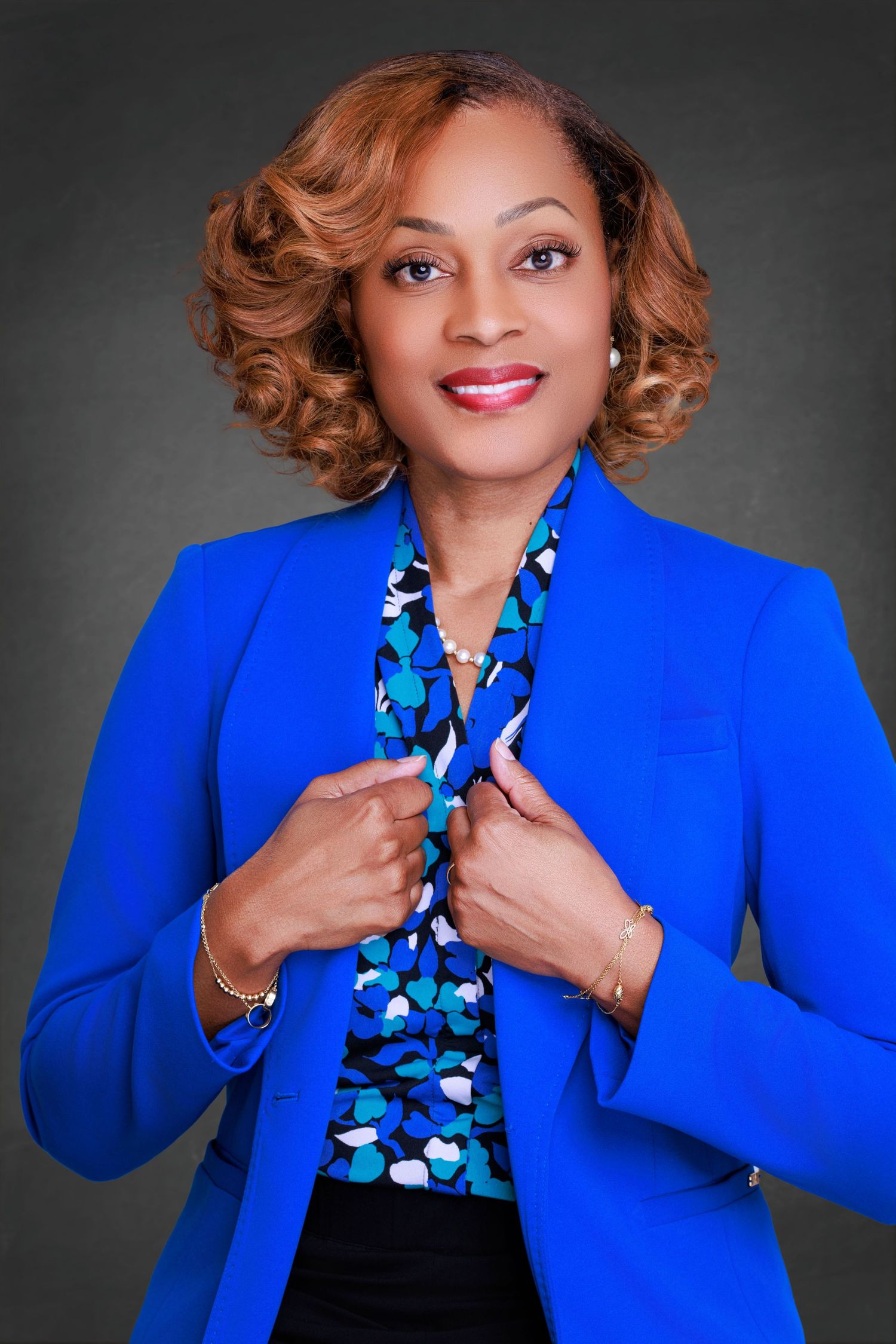 Professional headshot of a smiling woman with shoulder-length brown hair, wearing a blue blouse against a neutral background.