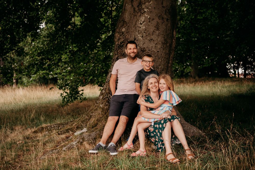 A loving family sits together outdoors for a photo session in a natural setting with tall grass and trees.