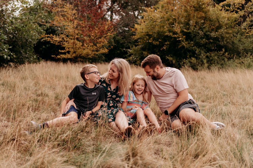 Family sitting together in a golden autumn field with tall grass and fall foliage in the background.