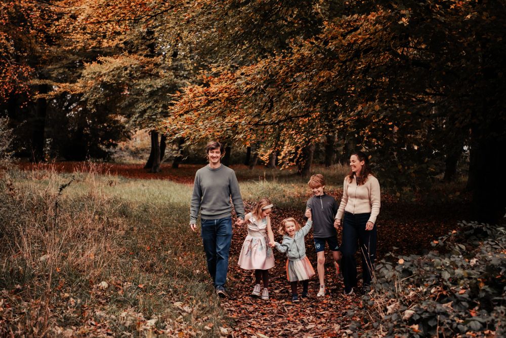 A group takes an autumn stroll together through a wooded park with orange and brown fall foliage overhead.
