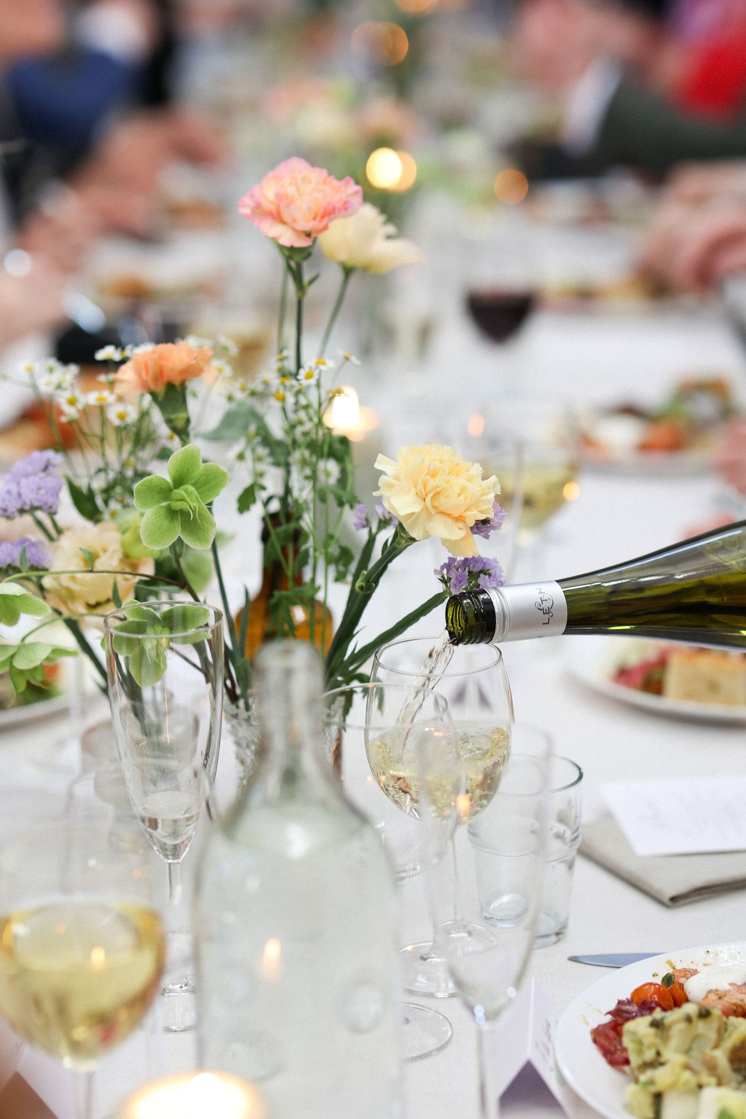 Elegant wedding reception table setting with champagne being poured and floral centerpieces.