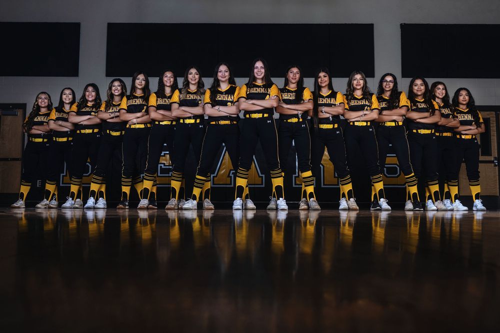 Athletic team in yellow and black striped uniforms pose together for official team photo on hardwood floor.