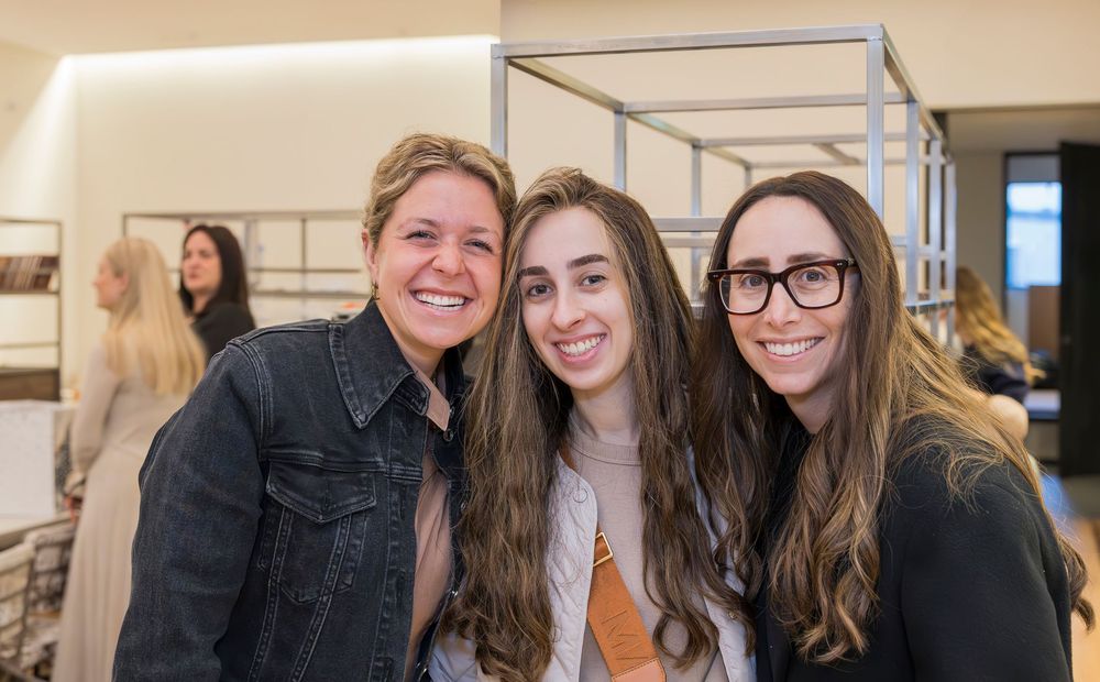 Three people smile together at an indoor event while wearing casual attire.