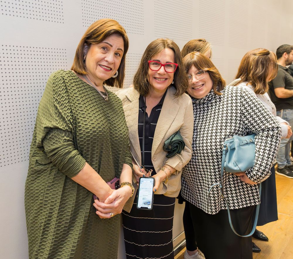Three people stand together smiling at a social gathering, wearing casual business attire in green and neutral tones.