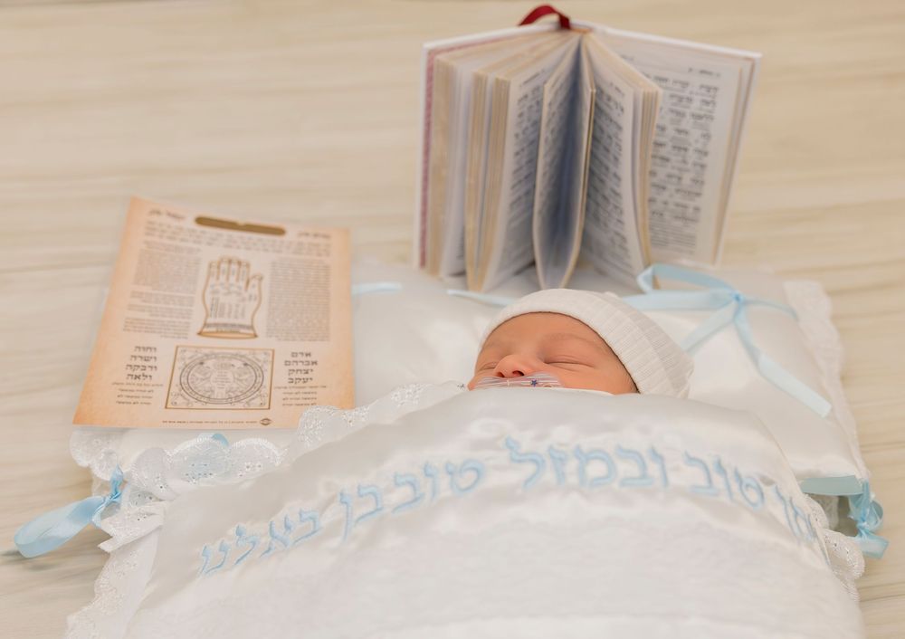 Baby wrapped in white cloth with blue ribbons lies next to a prayer book and religious documents.