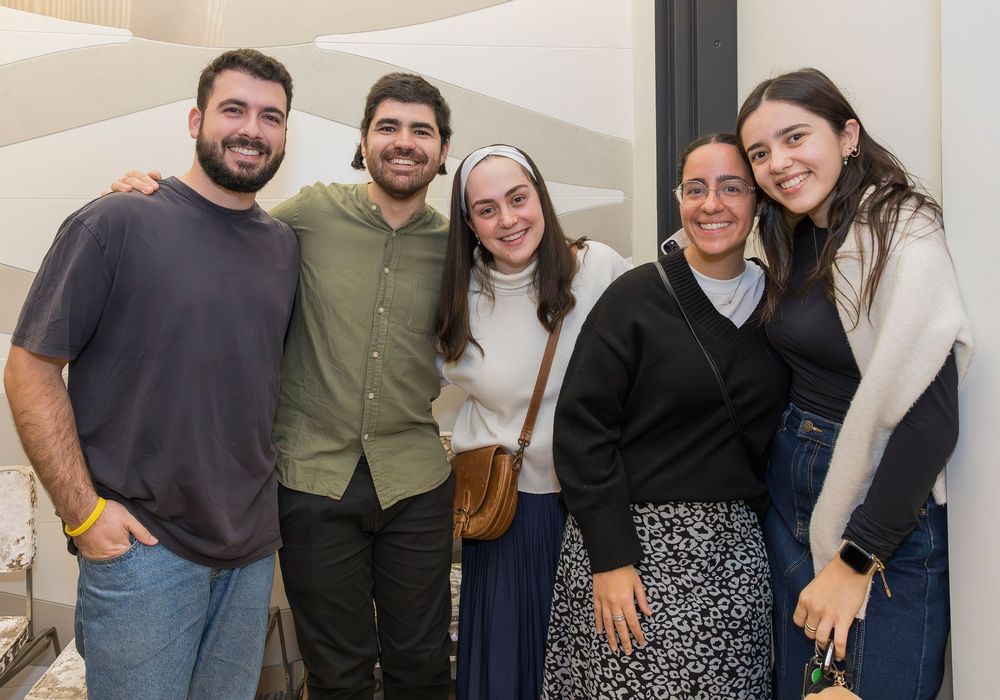 A group of five people standing together indoors, smiling warmly at the camera in casual attire.