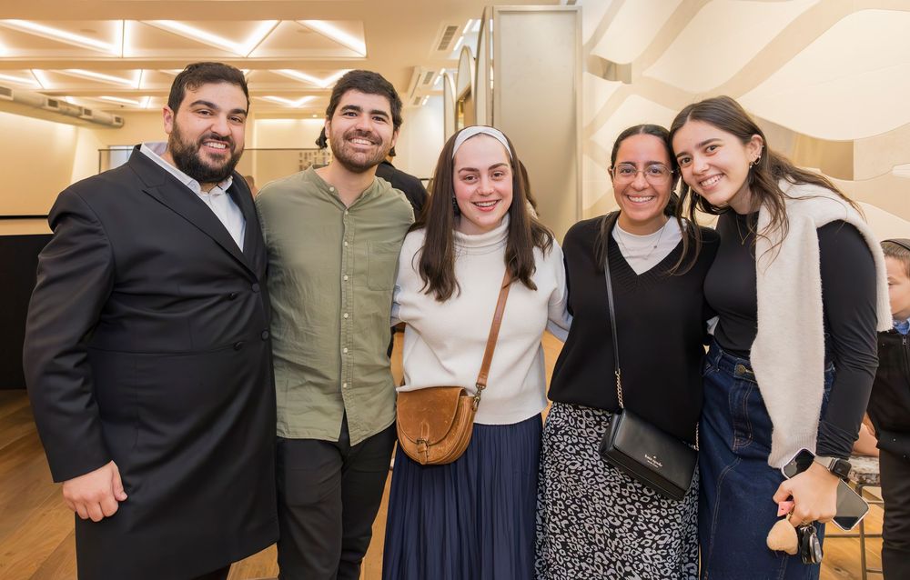 A group of five friends stand together smiling in a brightly lit indoor setting.