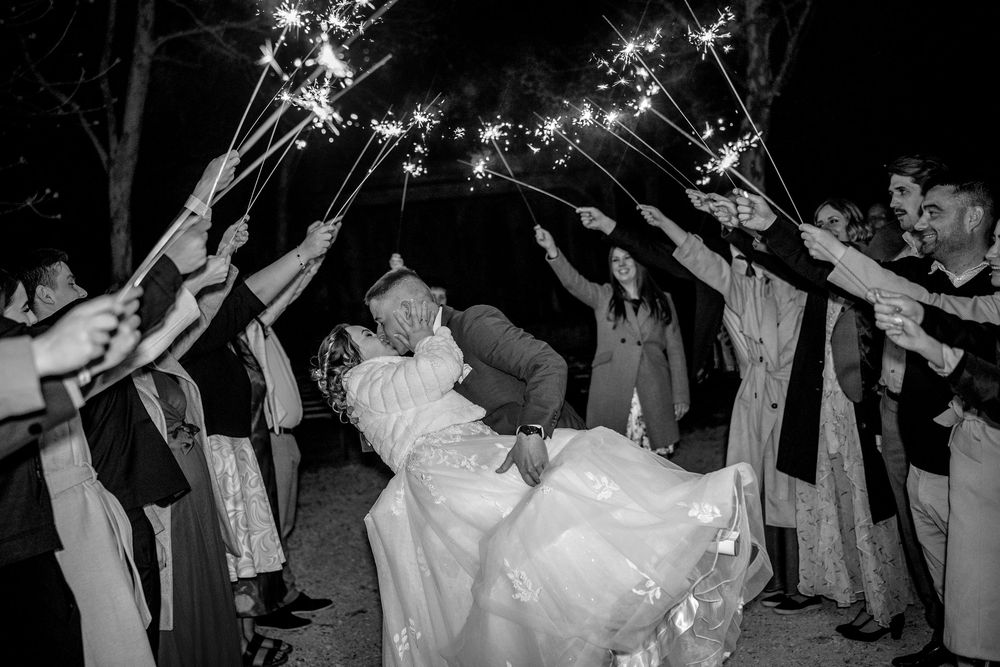 Wedding guests create a magical sparkler exit tunnel for newlyweds in elegant black and white photography.