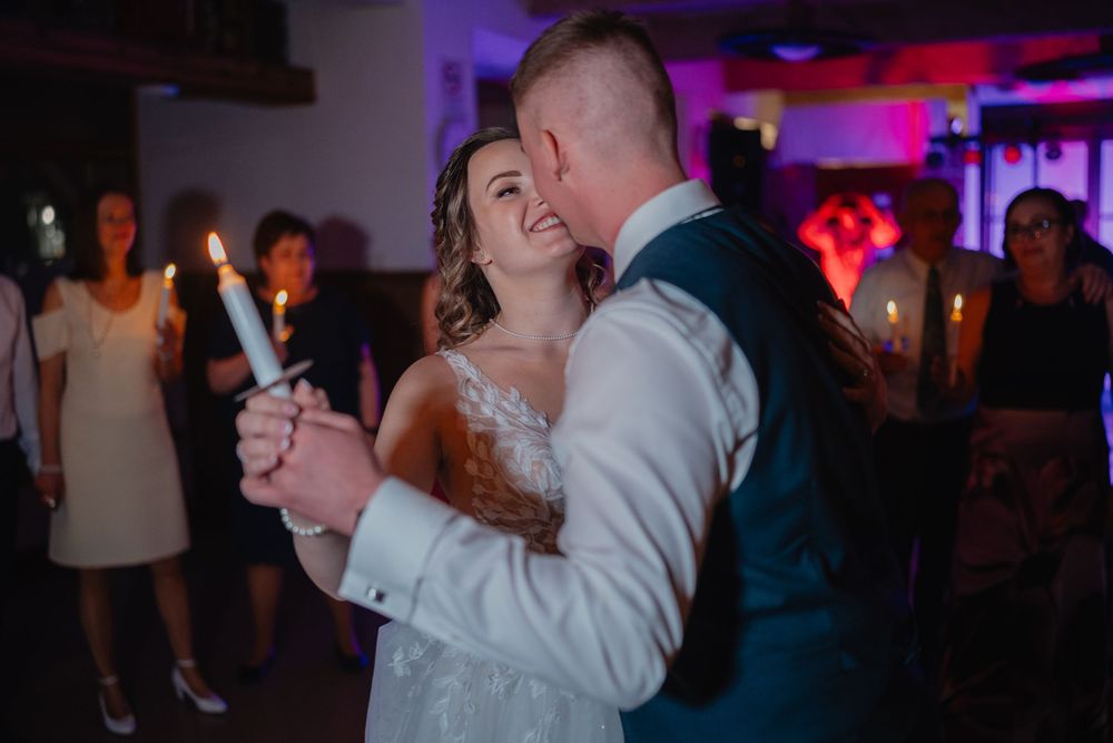 A couple dances together holding candles while celebrating at a dimly lit wedding reception.