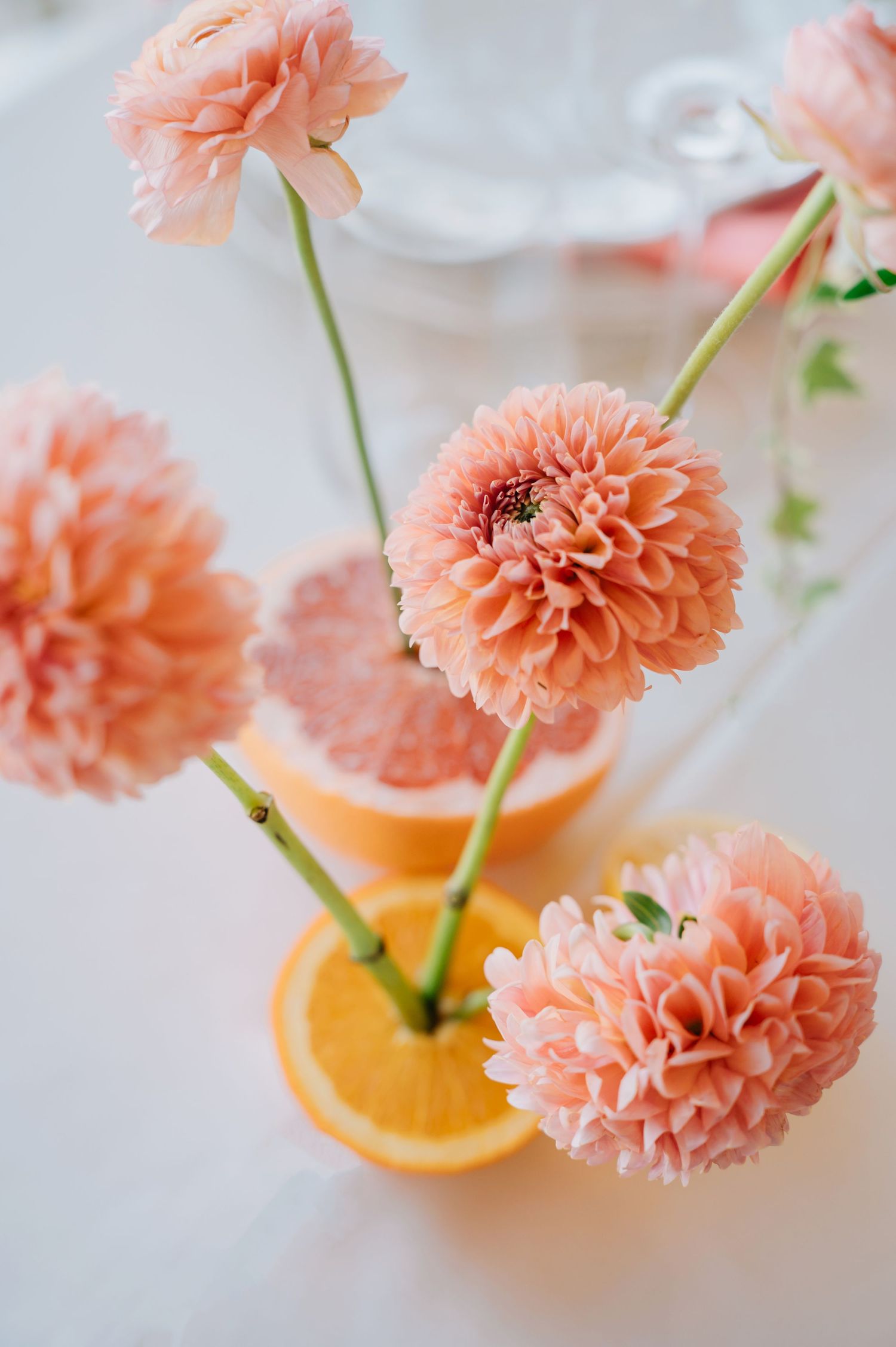 Beautiful peach-colored dahlia flowers arranged in a sliced orange decorative vase against a light background.