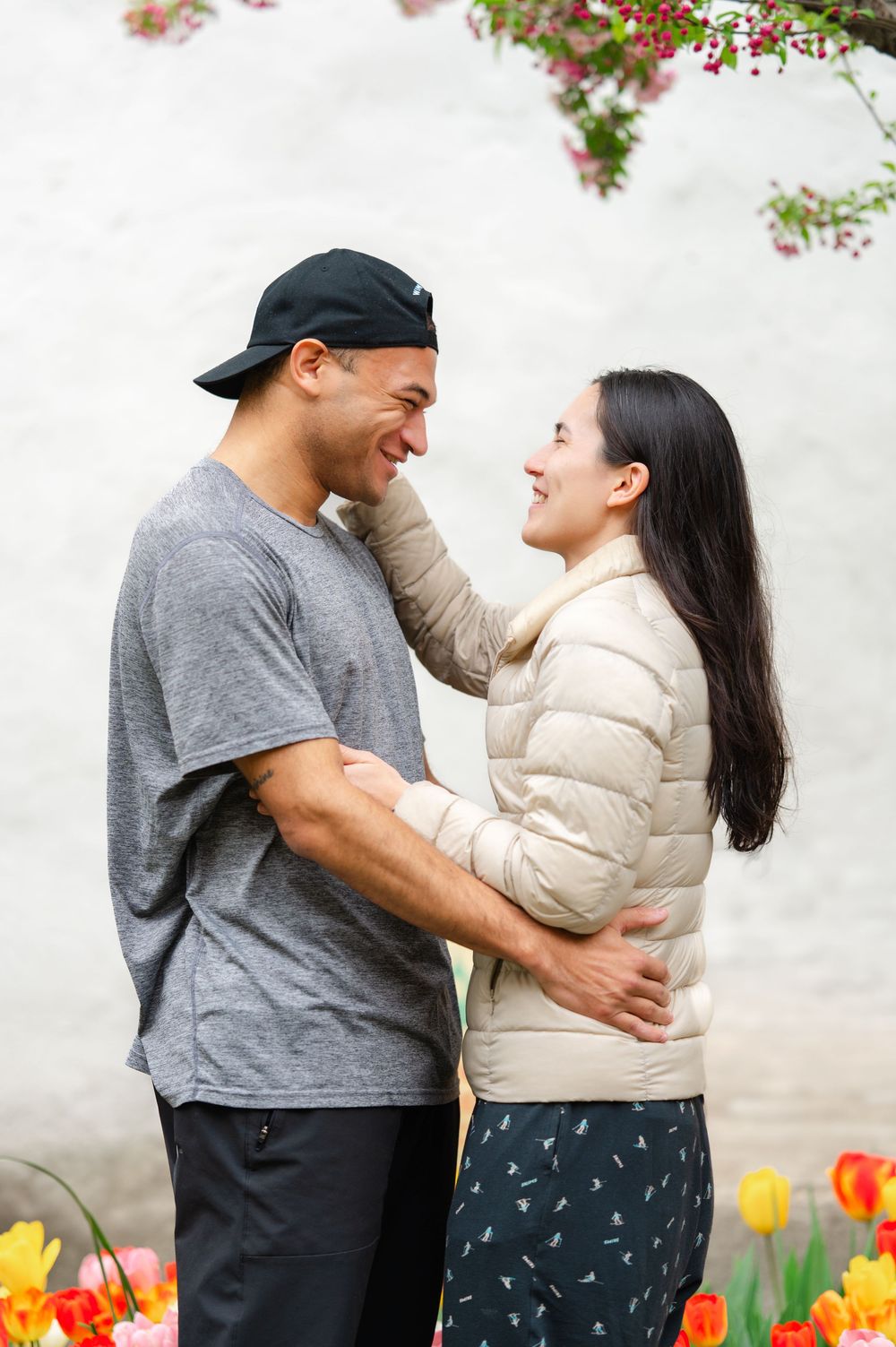 A couple shares a joyful moment together while standing in a garden with colorful tulips blooming during an engagement session in NYC