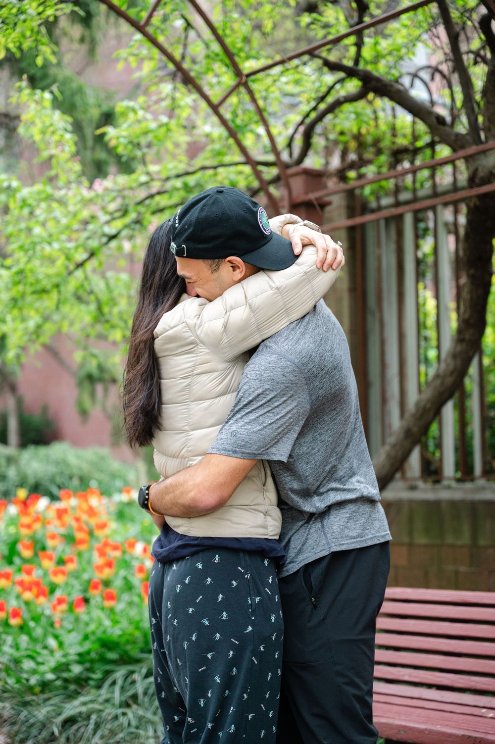 A couple embraces in the Westside Community Garden on the UWS with orange tulips and spring foliage in the background after their proposal