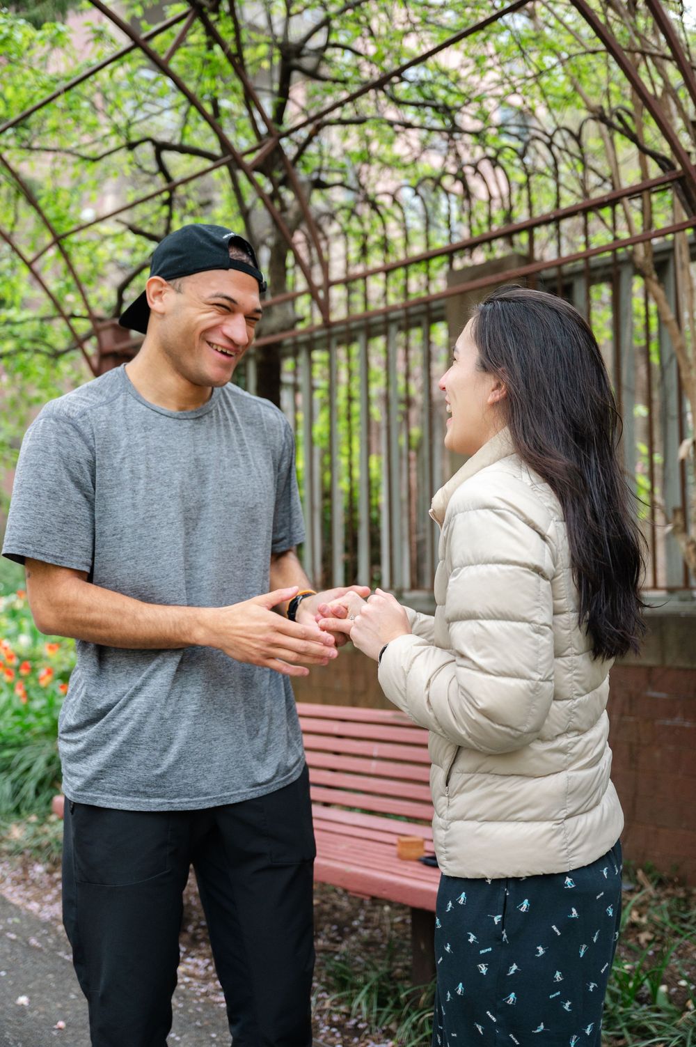 A couple sharing a joyful moment together in a garden setting with blooming trees and a wooden bench.