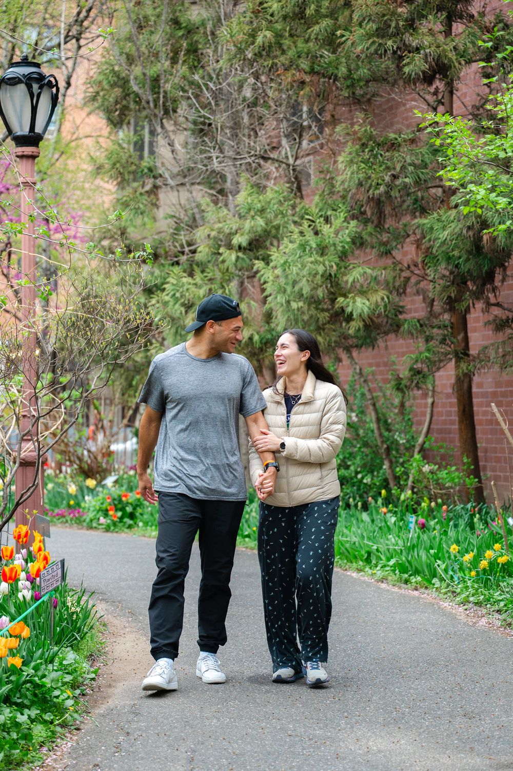A couple walks together on a garden path lined with spring flowers and trees in the Westside Community Garden on the UWS