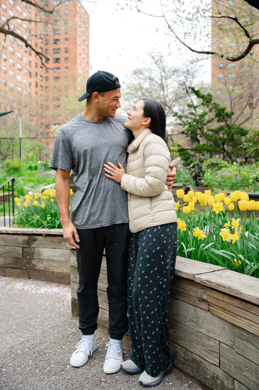 Couple sharing a tender moment while standing near blooming yellow tulips and spring flowers in the Westside Community Garden on the UWS
