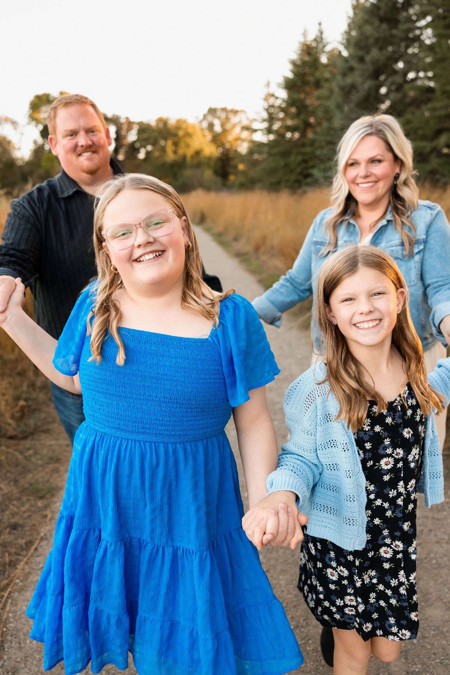 Family photo taken outdoors at golden hour with two children and two adults on a grassy trail.