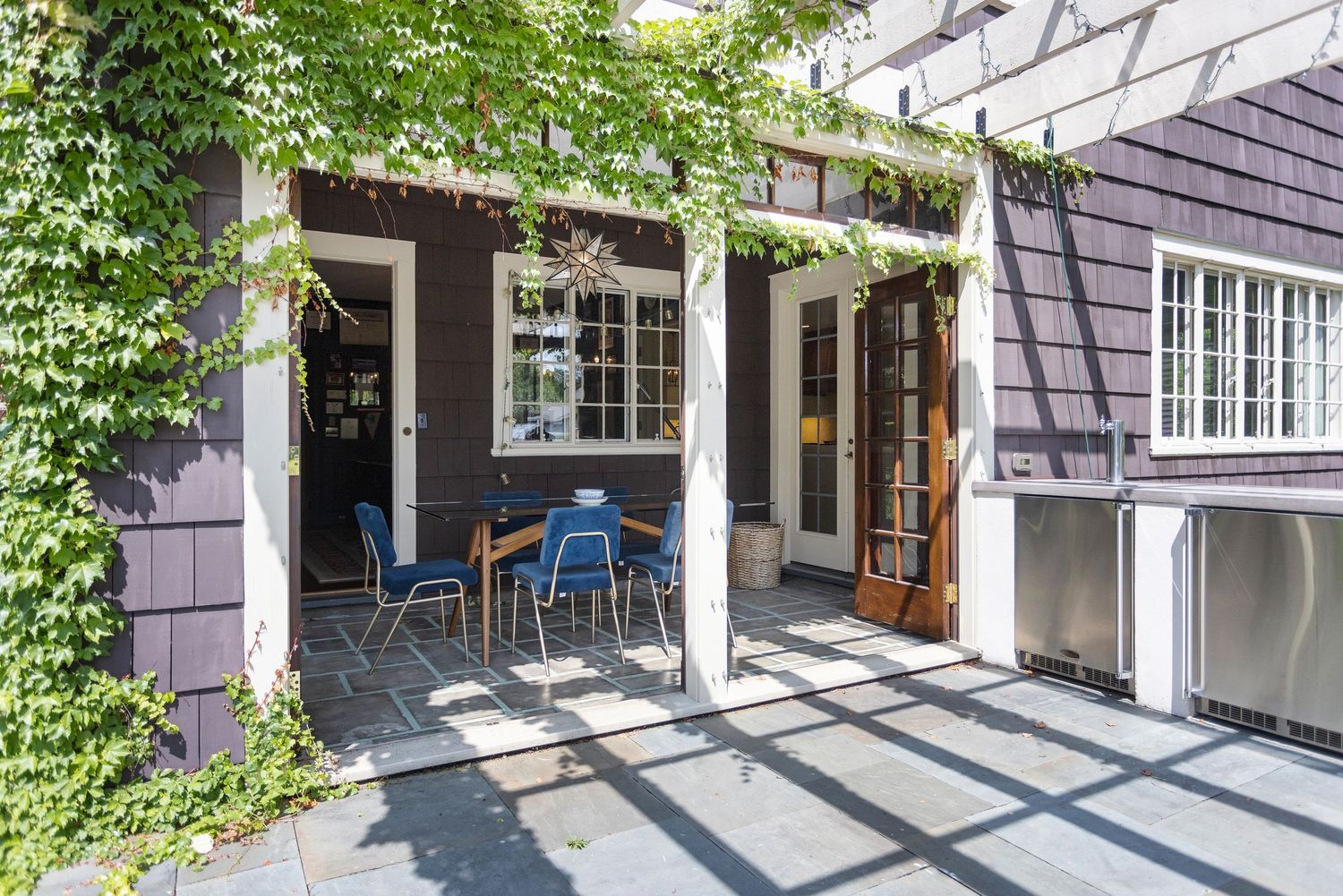Charming patio with pergola, ivy-covered walls, outdoor dining area, and built-in stainless appliances for stylish alfresco living.