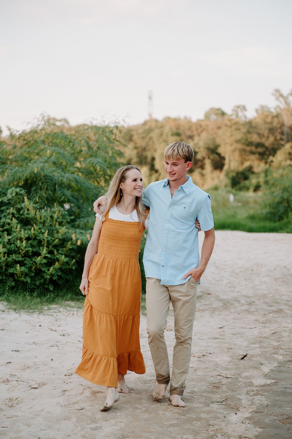 Couple walking together on sandy path at sunset, wearing yellow maxi dress and light blue shirt.