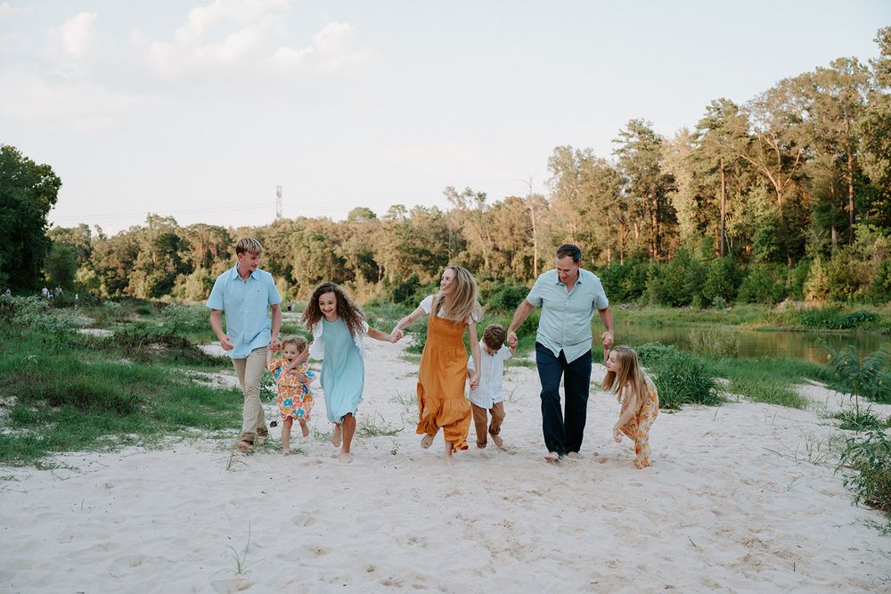 A group walks together with dogs on a sandy path surrounded by green trees during golden hour.