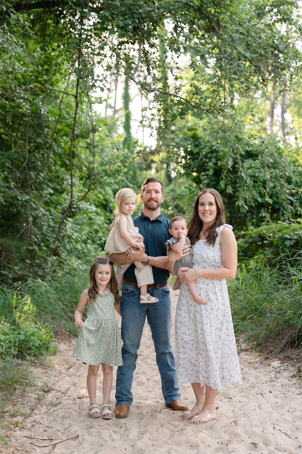 A group stands together on a sandy forest path surrounded by lush green foliage on a bright summer day.