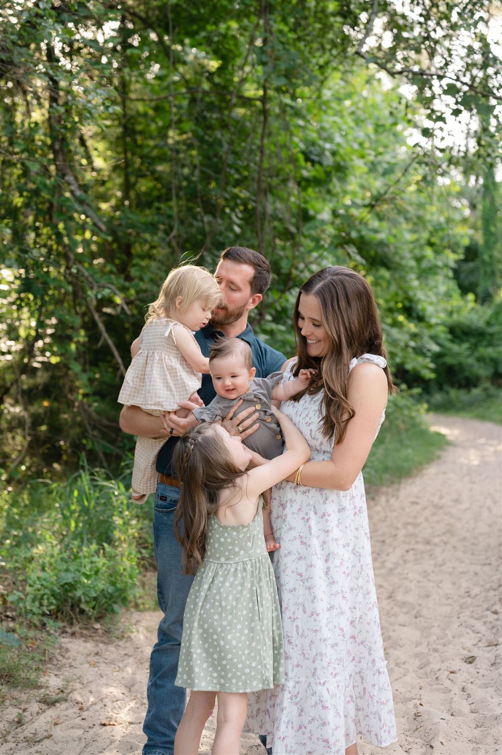 A family shares a tender moment together while standing on a dirt path surrounded by lush green foliage.