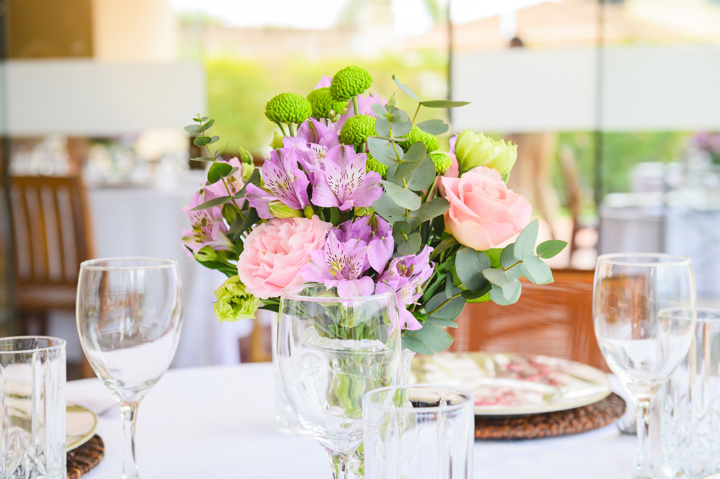 Table setting with pink and purple floral centerpiece in glass vase alongside elegant wine glasses and place settings.