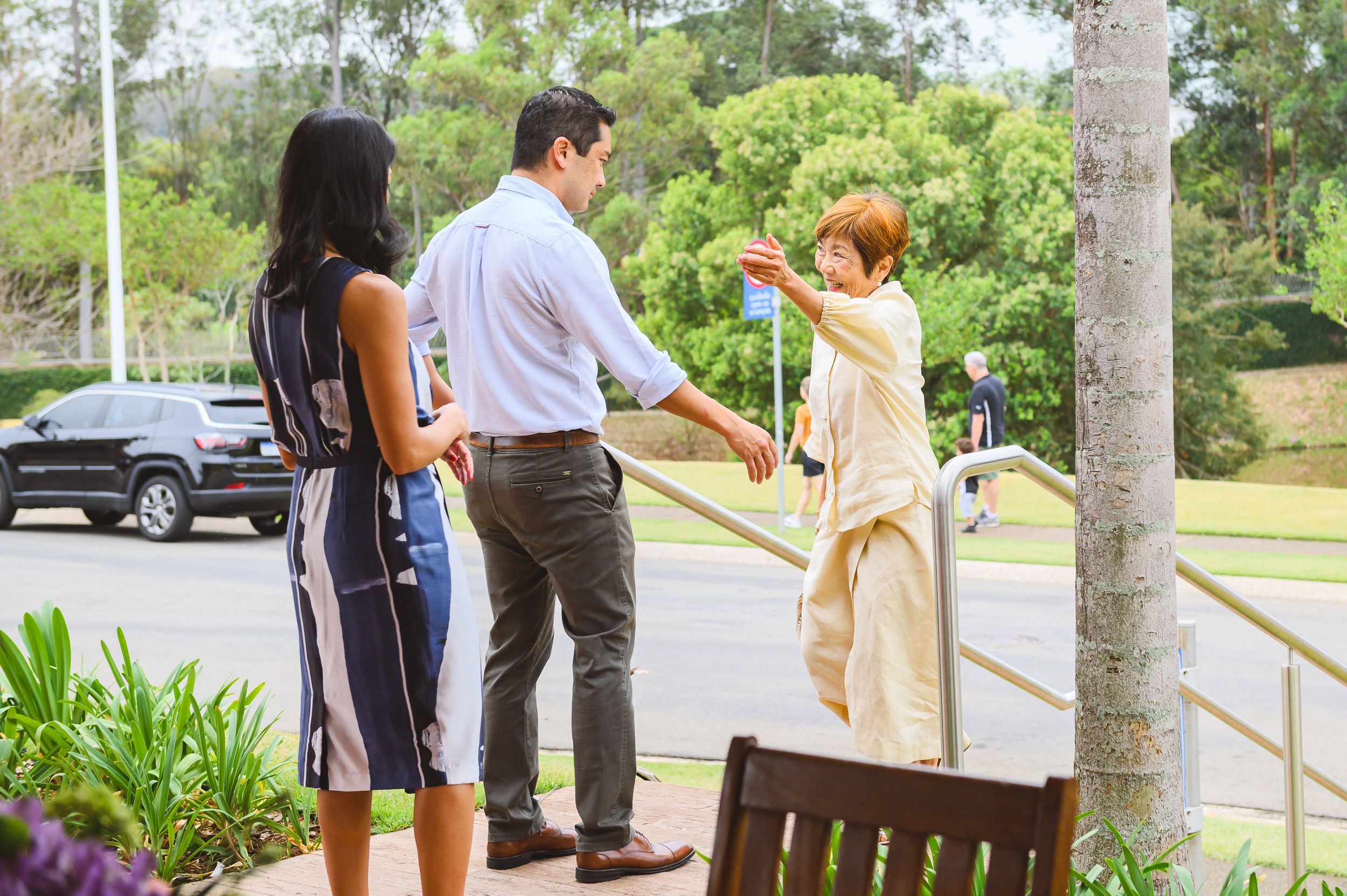 Three people having a professional conversation outdoors near a palm tree and parking area.