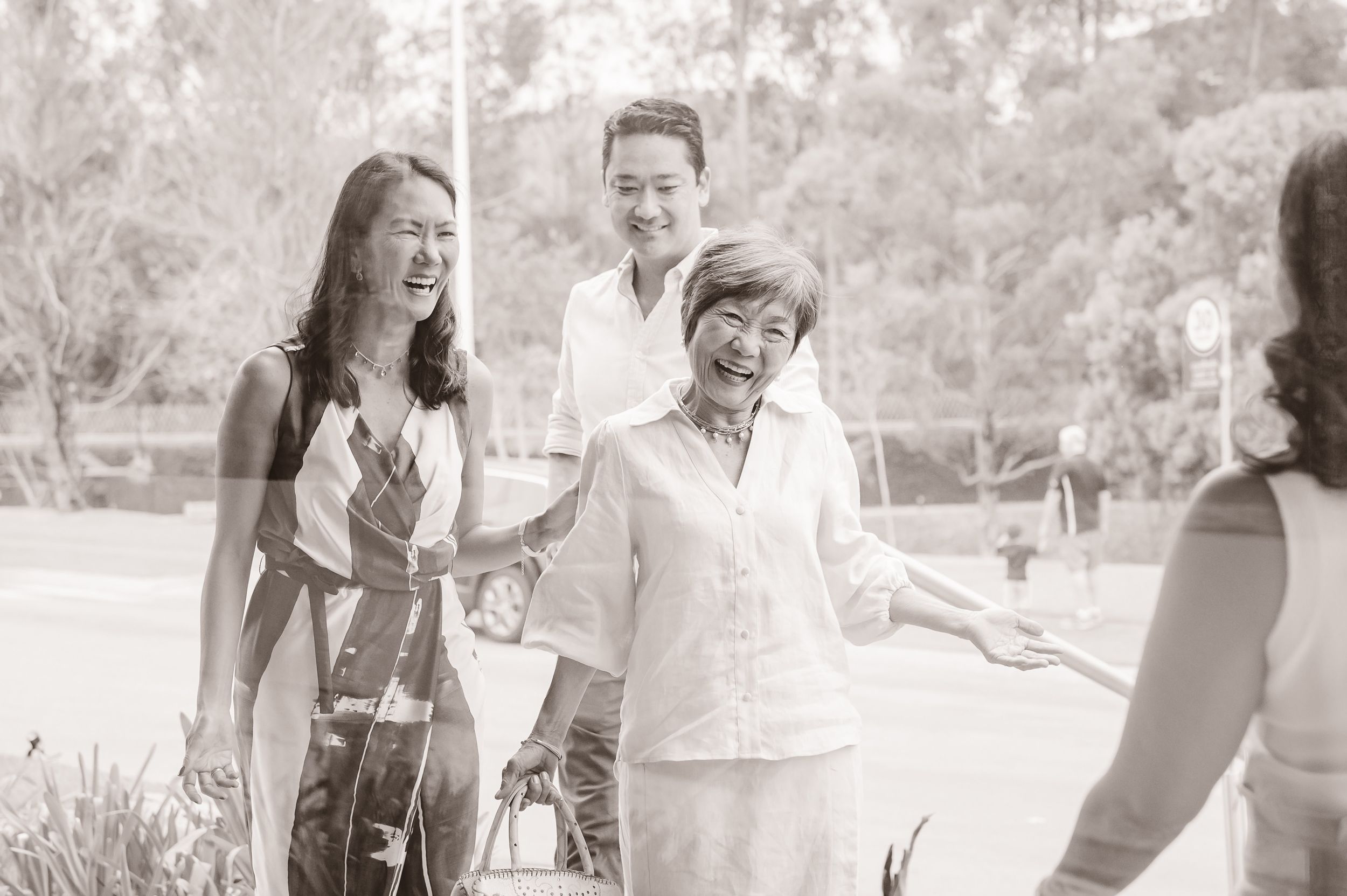 Three well-dressed family members enjoy a casual outdoor gathering on a bright sunny day.