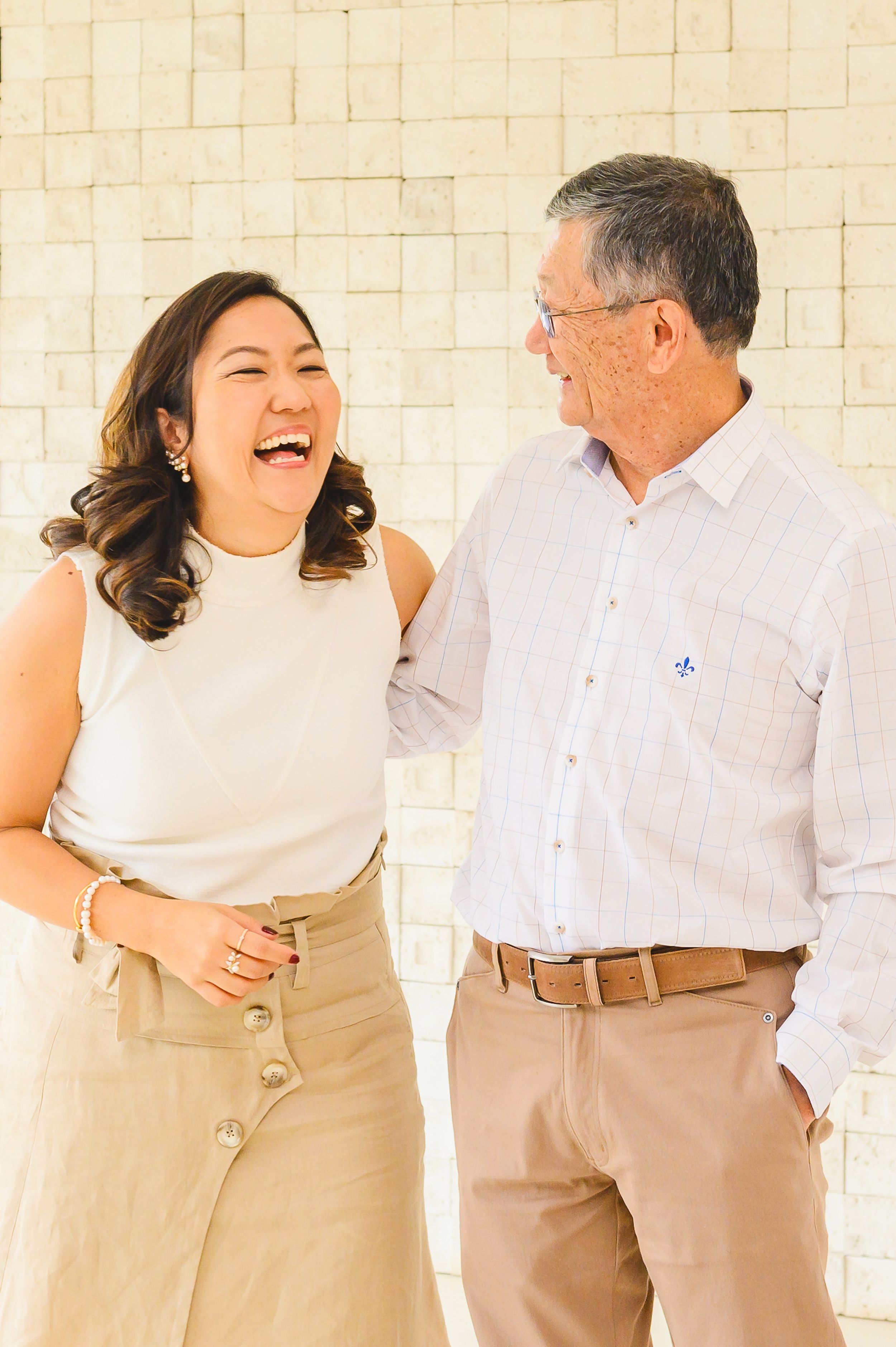 A joyful moment shared between two people wearing neutral tones while standing against a light textured wall.