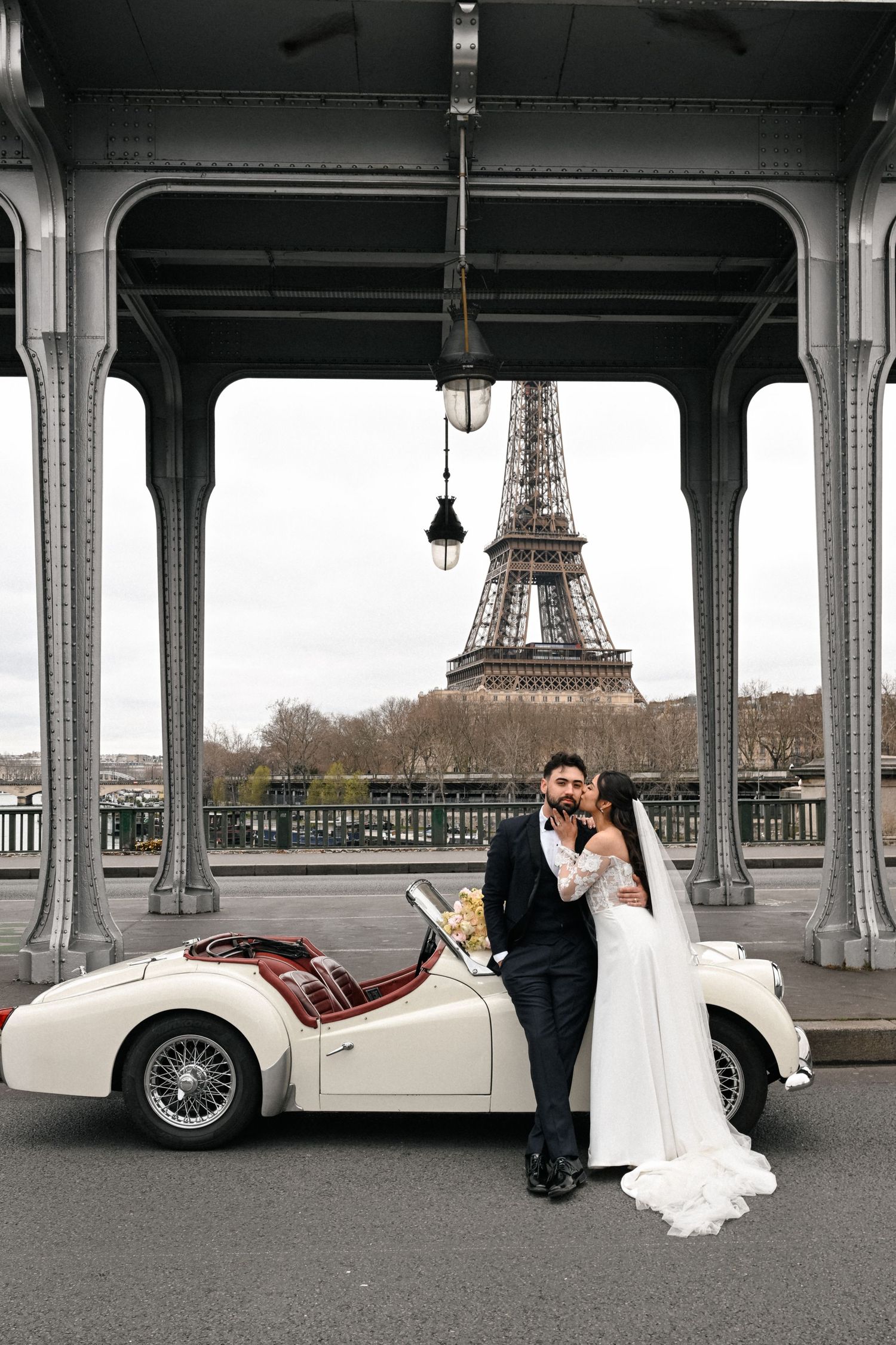 Stylish couple poses under arched colonnade with palm trees visible in background, captured in black and white.