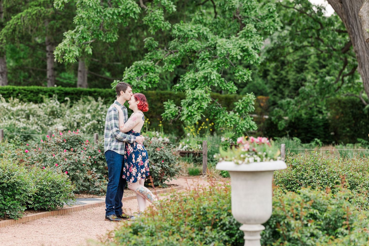 A romantic outdoor garden scene with a couple embracing near a decorative stone urn along a landscaped pathway at Cantigny Park