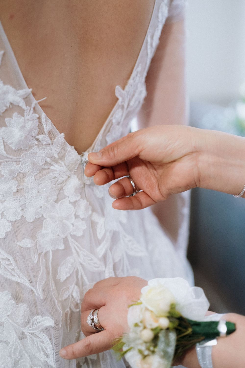 Close-up of hands adjusting delicate lace details on a white wedding dress.
