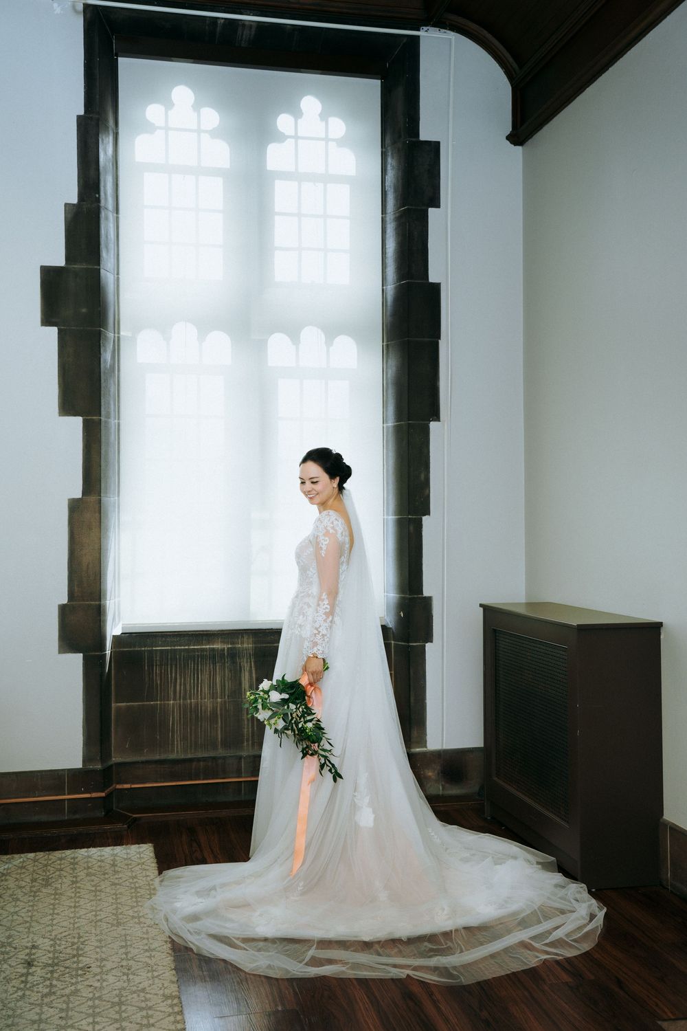 Bride in lace wedding gown poses by Gothic window in elegant church interior.