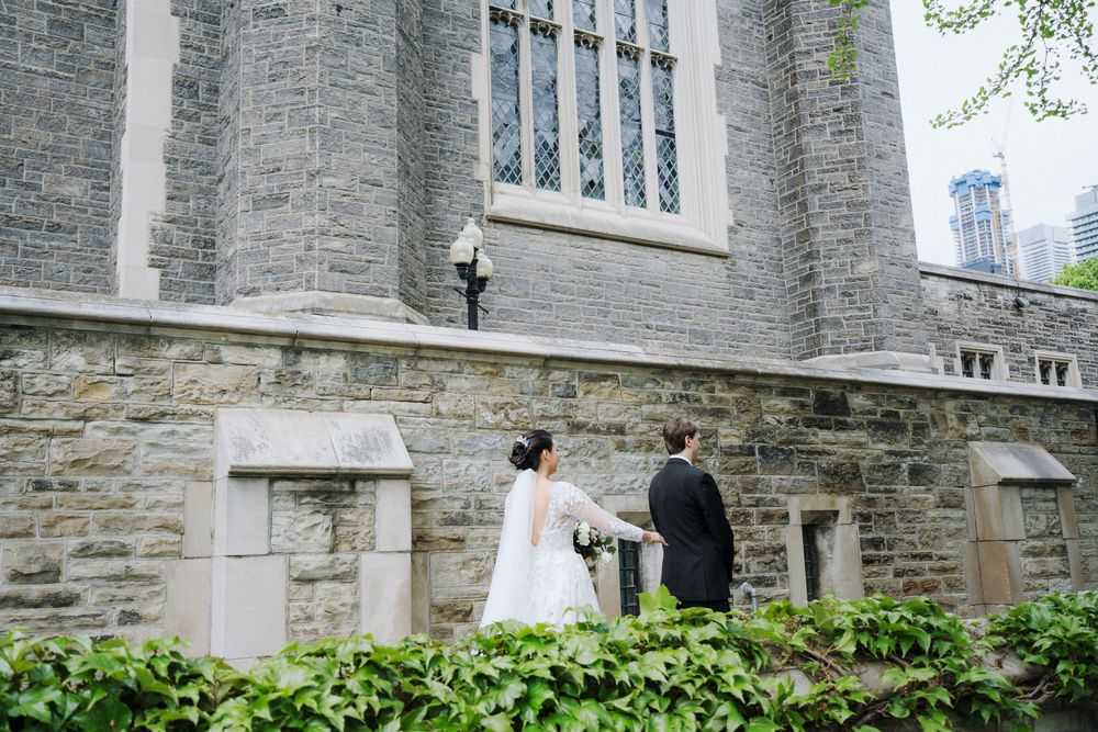 Bride and groom walking outside Gothic stone church building with elegant architectural details.