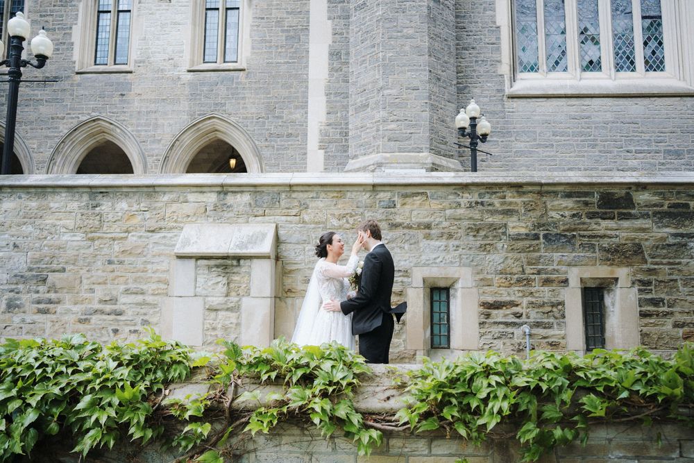 Couple in wedding attire embracing on stone steps of historic church building.