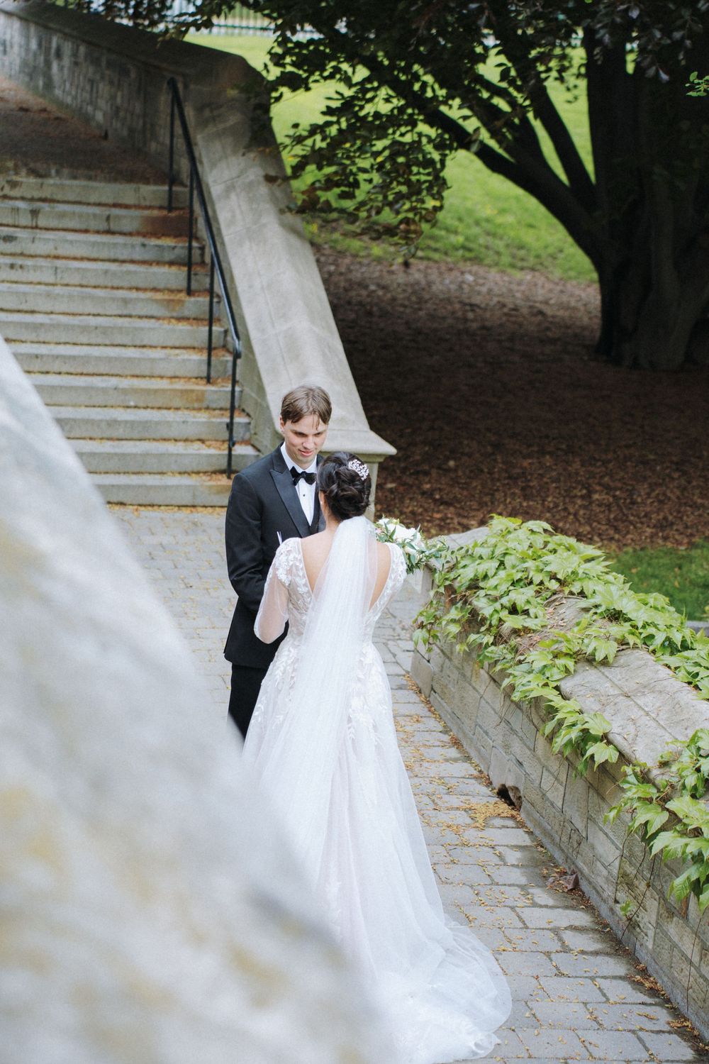 Wedding couple on stone stairway under trees sharing intimate moment.