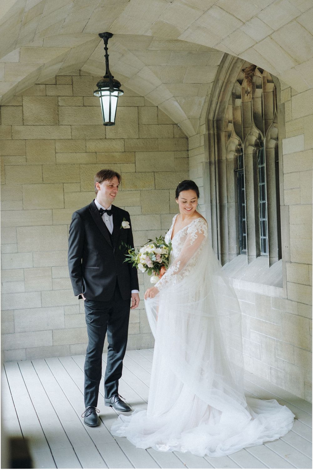 A wedding couple takes romantic first look photos under a stone archway corridor.