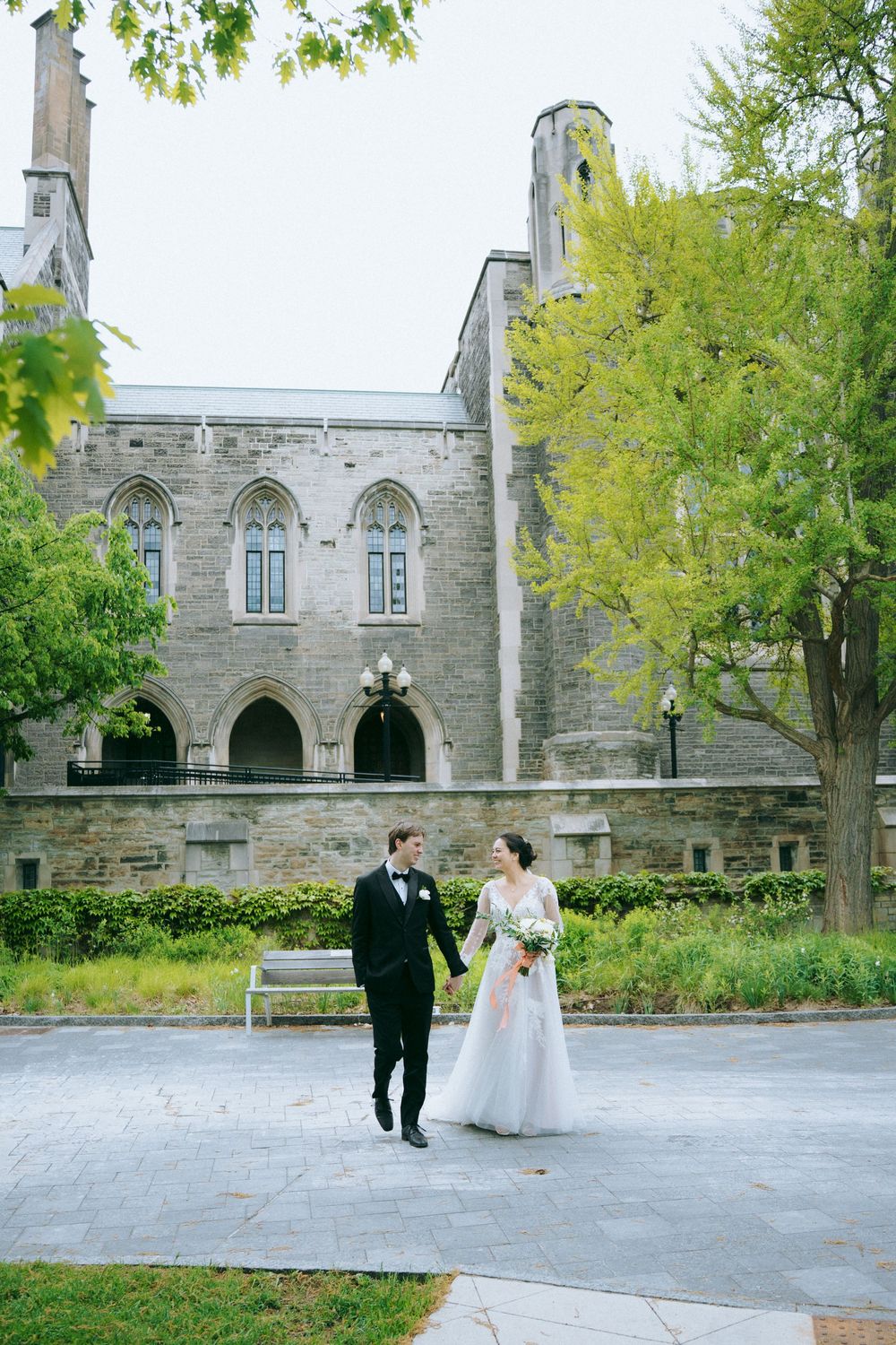 Wedding couple walks together on grounds of historic stone church building.