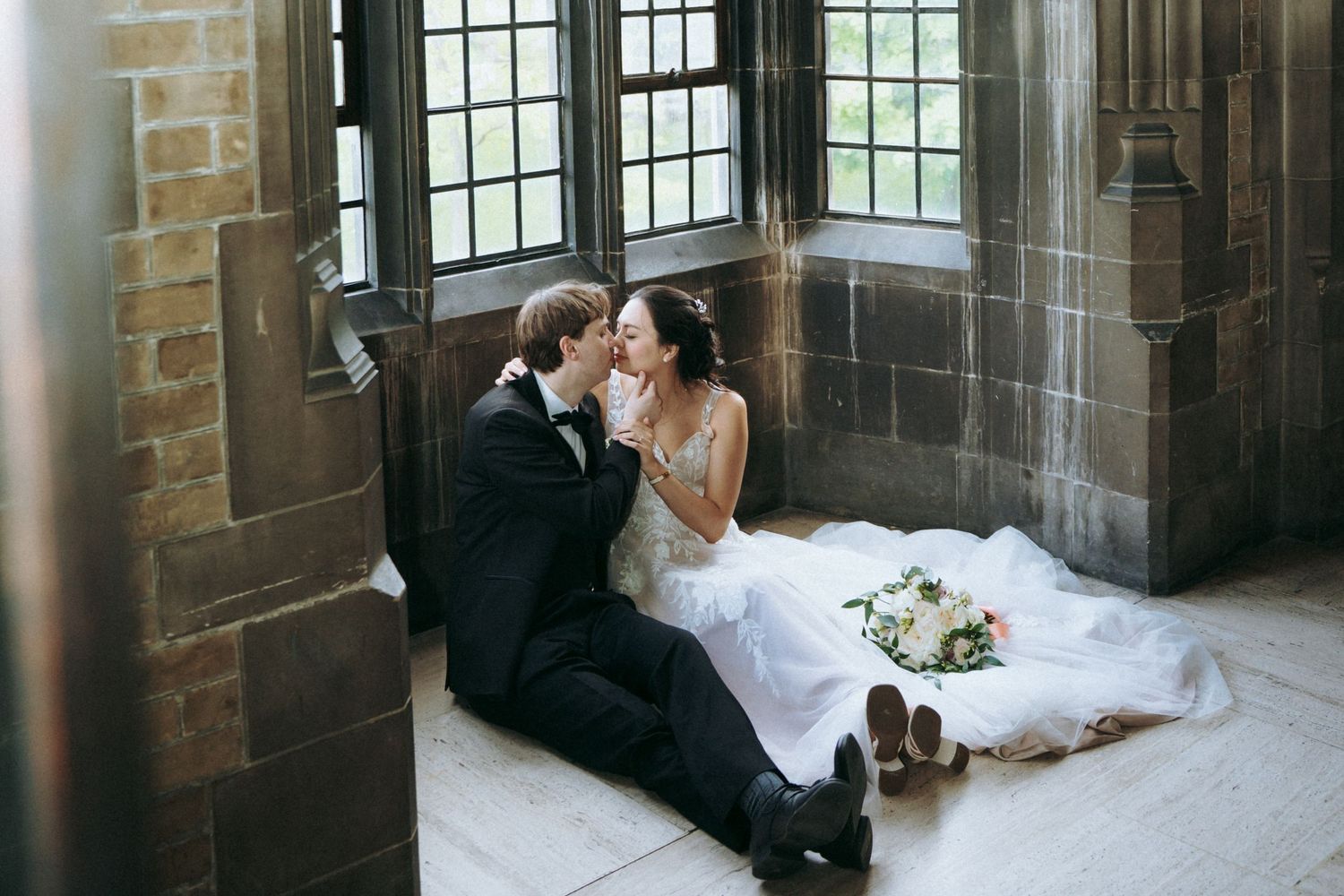 Couple shares intimate moment sitting by gothic window in historic stone building.