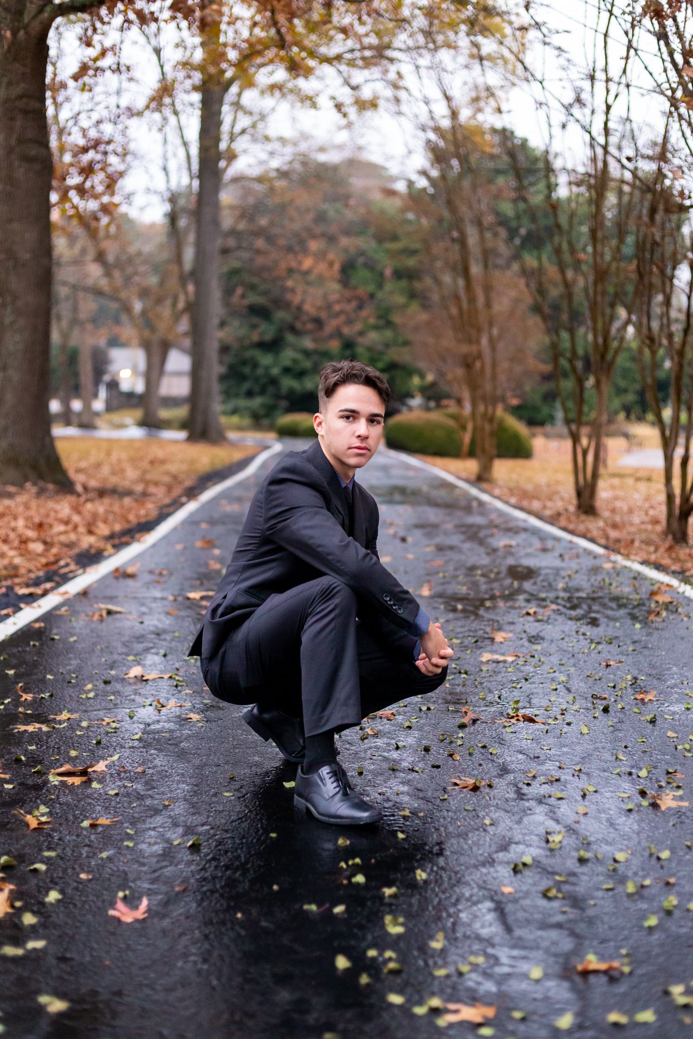 male teen crouched down on a rain soaked road, posing for senior pictures with MegMc Photography, Medina, TN