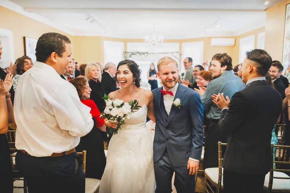 Joyful newlyweds exiting their ceremony surrounded by celebrating guests in a bright indoor venue at Josephine Butler Parks Center