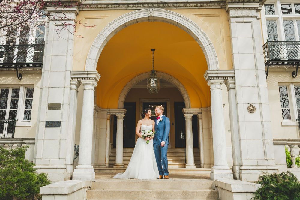 Elegant wedding ceremony under a stone archway colonnade with yellow arched ceilings and white columns.