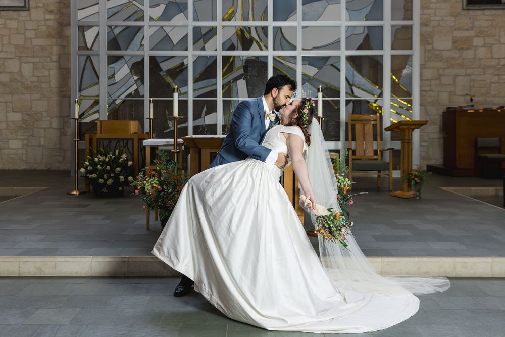 A romantic wedding scene showing a bride in a flowing white gown and veil kissing outside a church entrance.