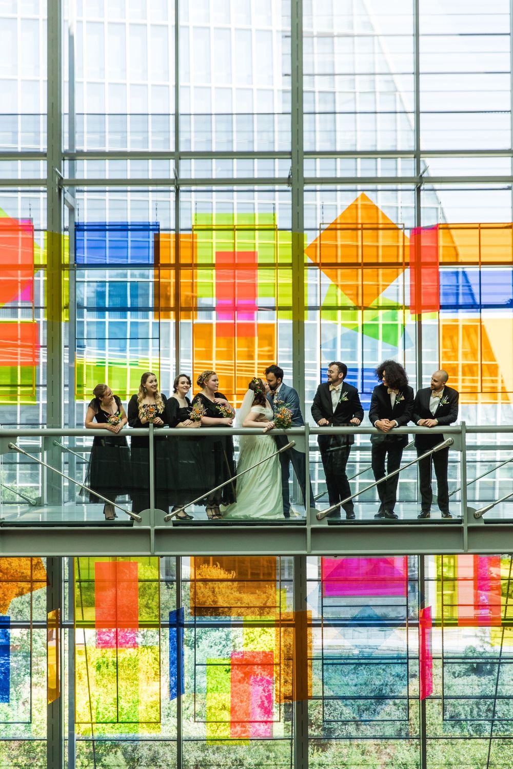 A wedding party stands on an elevated platform against a vibrant stained glass backdrop with colorful geometric patterns.